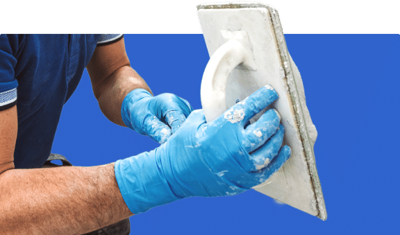 Worker wearing gloves applying plaster with a trowel.