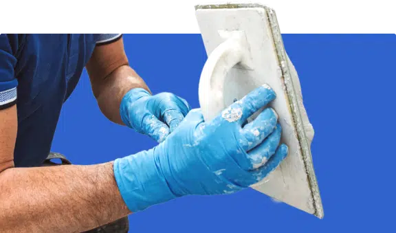 Worker wearing gloves applying plaster with a trowel.