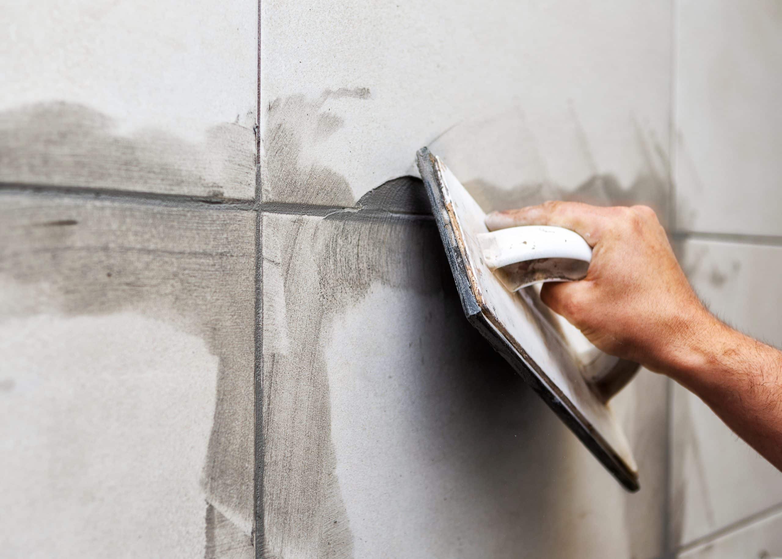 Applying fresh grout to bathroom wall tiles with a hand float.