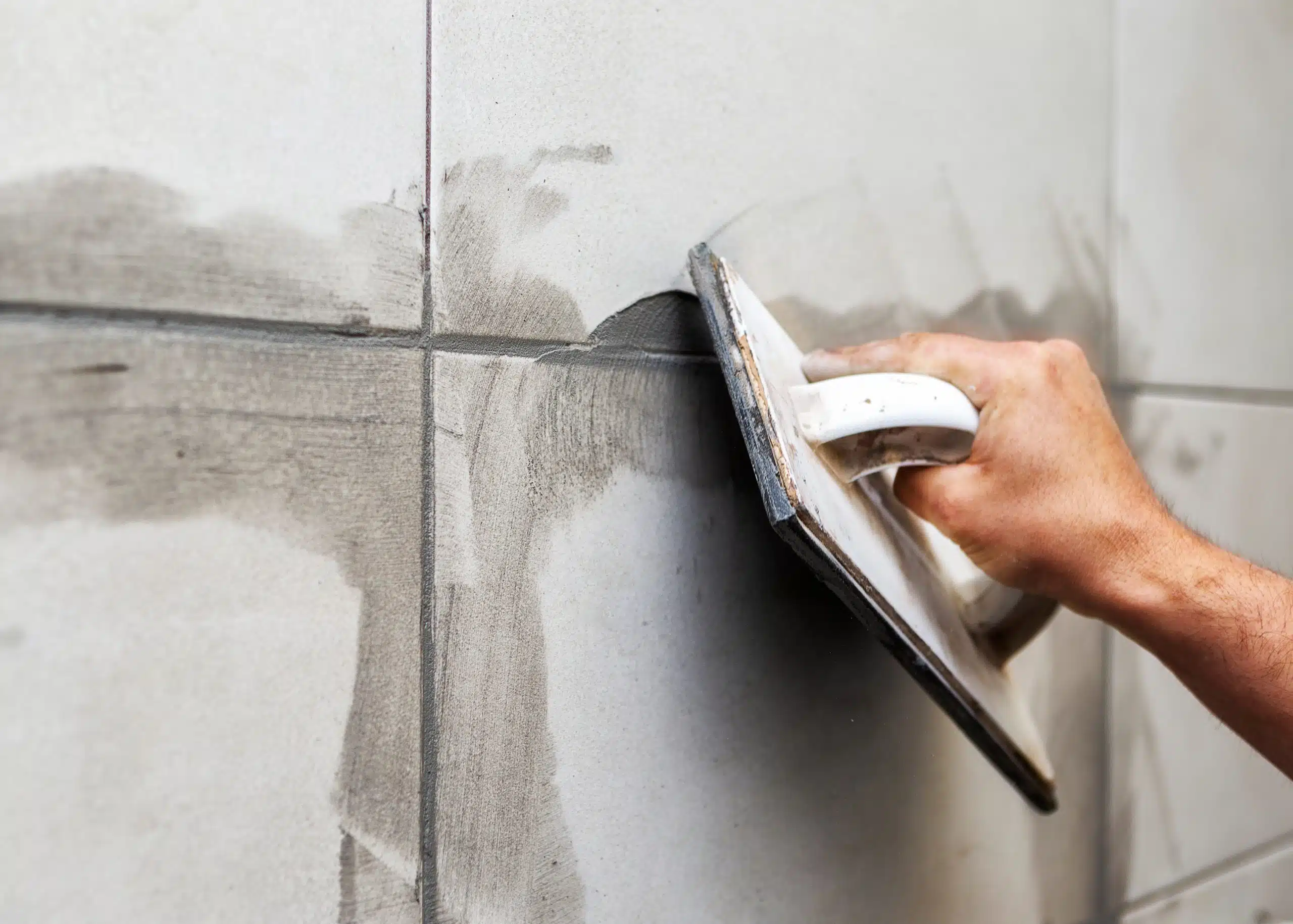 Applying fresh grout to bathroom wall tiles with a hand float.