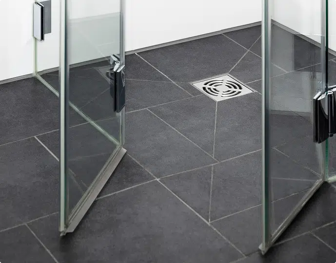 Shower floor with dark tiles, glass panels, and a central drain.
