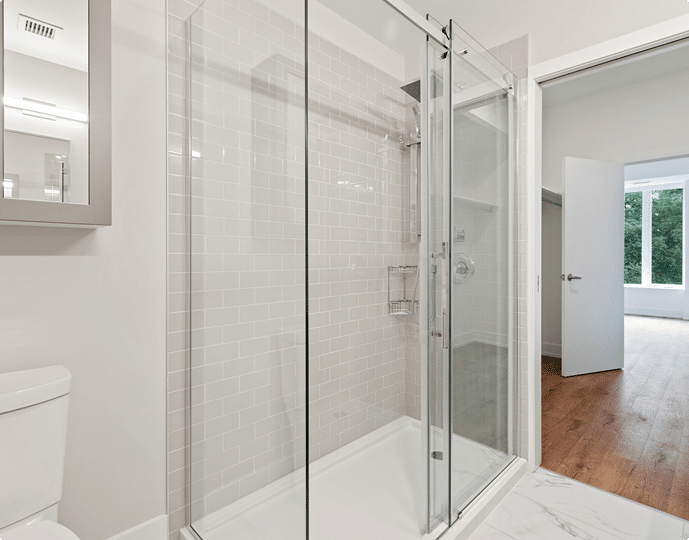 Modern bathroom with a glass shower enclosure, white tile walls, and a toilet.
