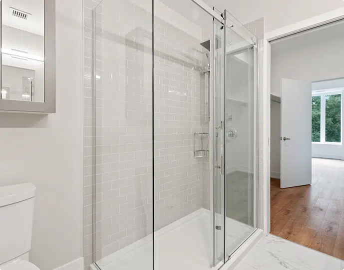 Modern bathroom with a glass shower enclosure, white tile walls, and a toilet.