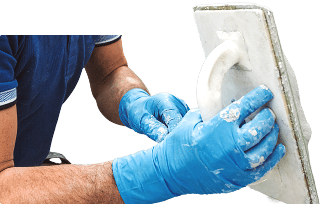 Worker wearing gloves applying plaster with a trowel.