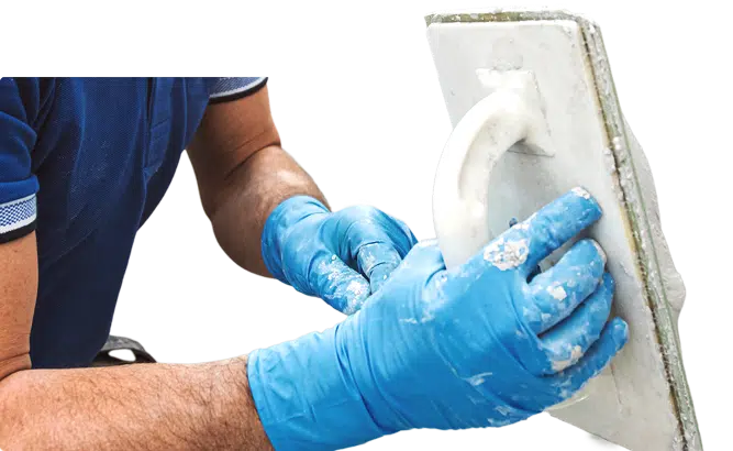 Worker wearing gloves applying plaster with a trowel.